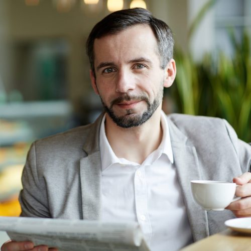 Happy businessman with paper and cup of coffee having break in cafe